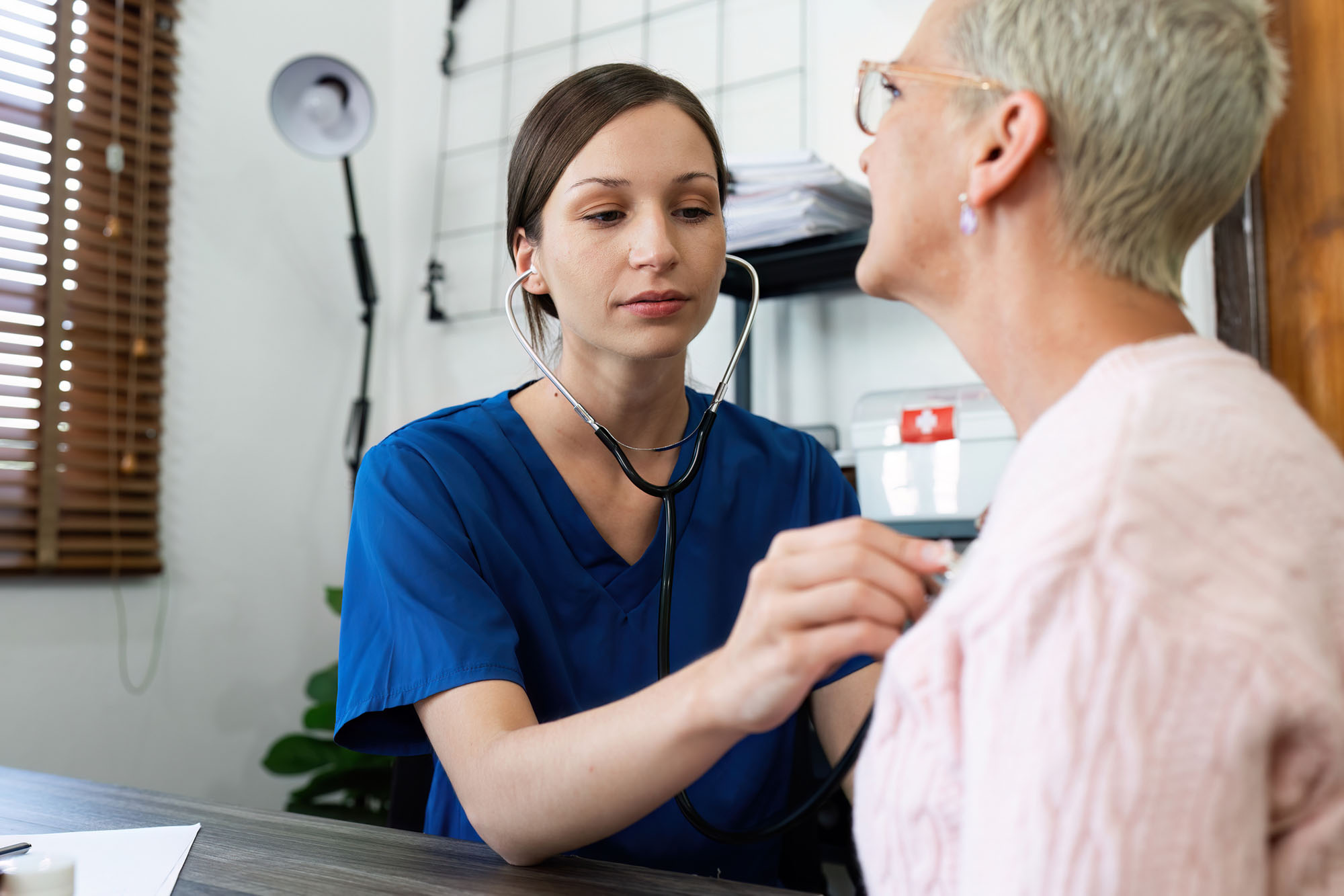 A healthcare provider listens to the heart of a senior female patient