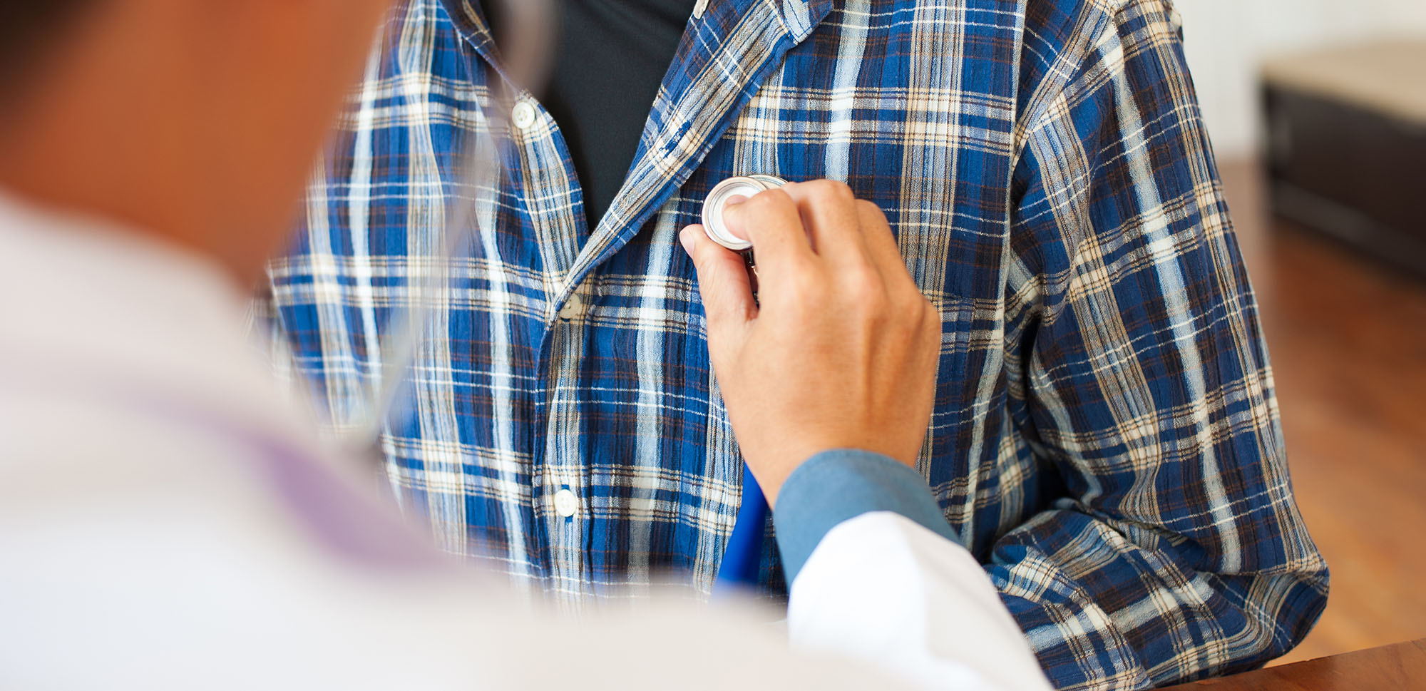 A doctor uses a stethoscope to listen to the heart of an adult man