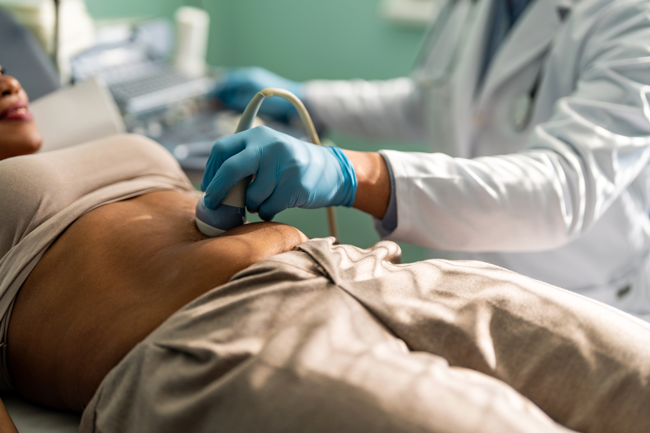 Gynecologist in sterile gloves using ultrasound scanner while examining female patient.