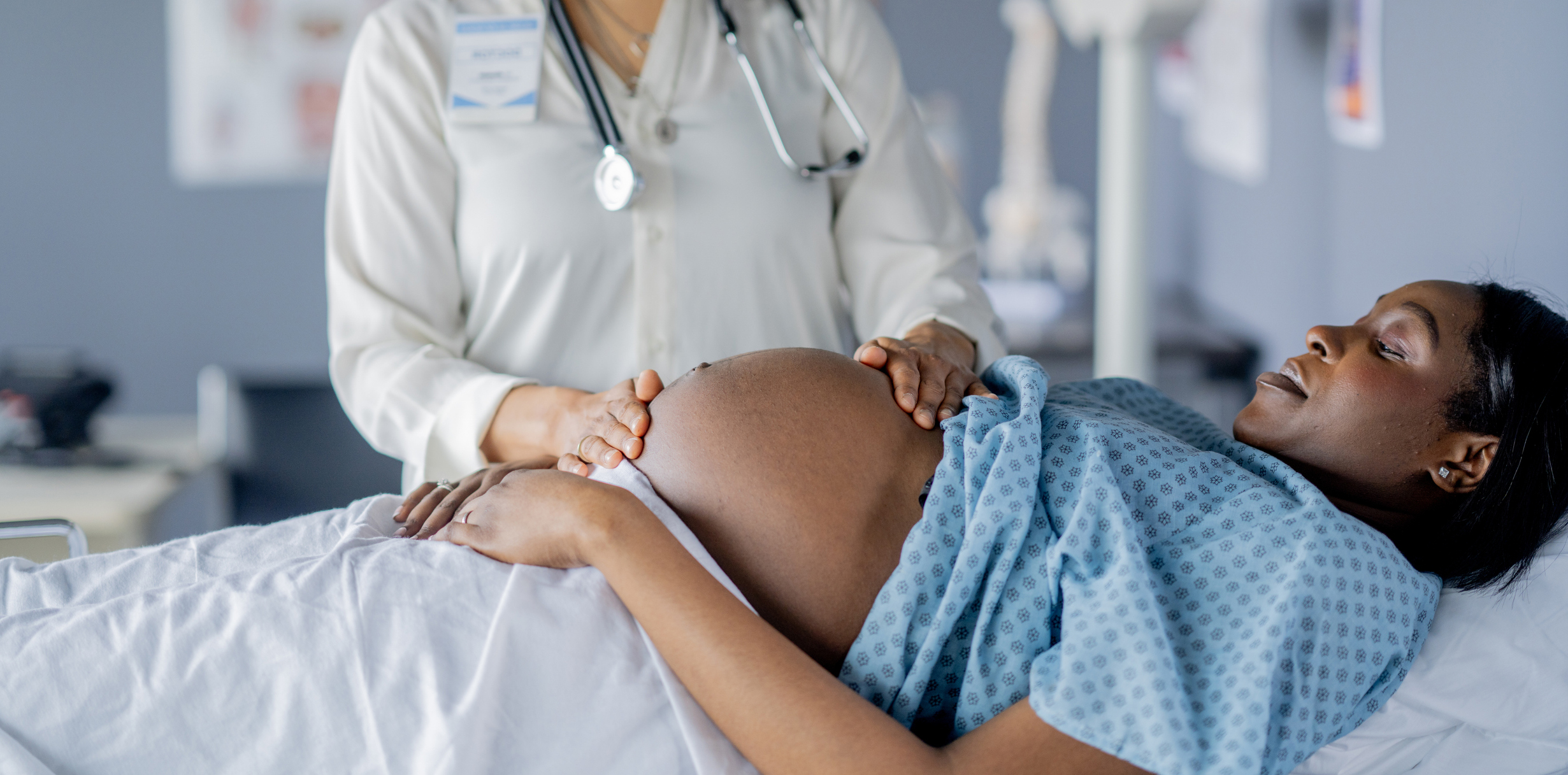 A pregnant woman lays out on an exam table during a prenatal appointment. Her Obstetrician is checking her growth and measuring baby's development.