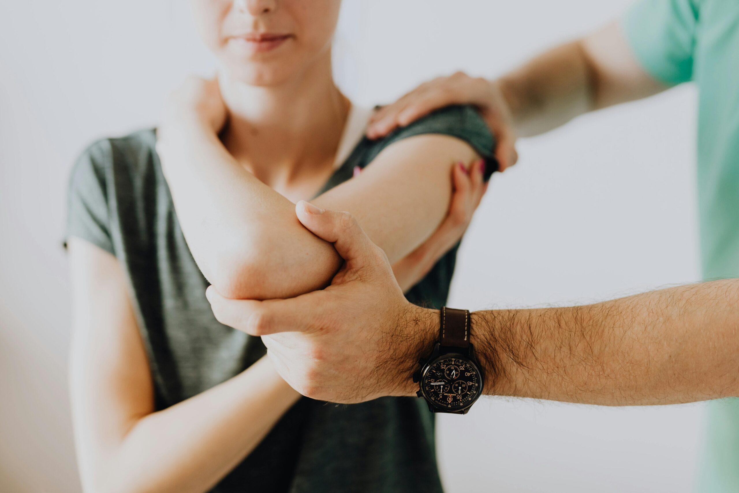 A provider out of frame helps a woman examine or stretch her shoulder.