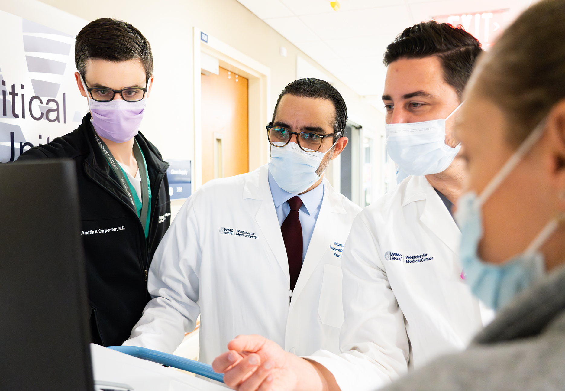 A team of neurosciences doctors confer over a patient at the computer.