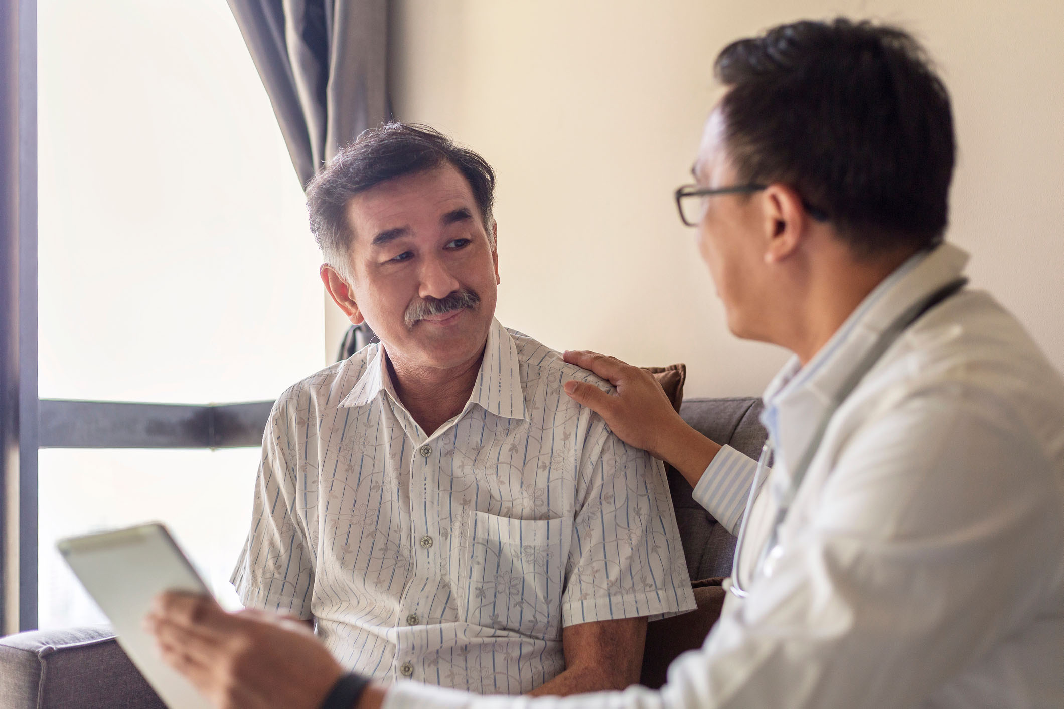 Smiling doctor consoling senior adult patient in medical clinic.