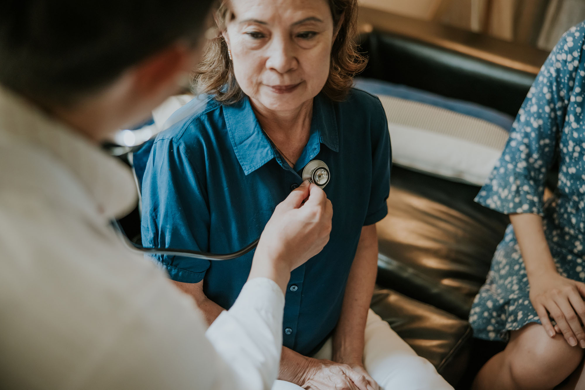 Asian Male doctor using a stethoscope to examining senior woman's lung and heartbeat during a healthcare visit.