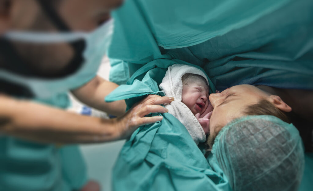 A baby born to a mother via C-section surgery. The healthy baby is placed next to the mother's face right after birth.