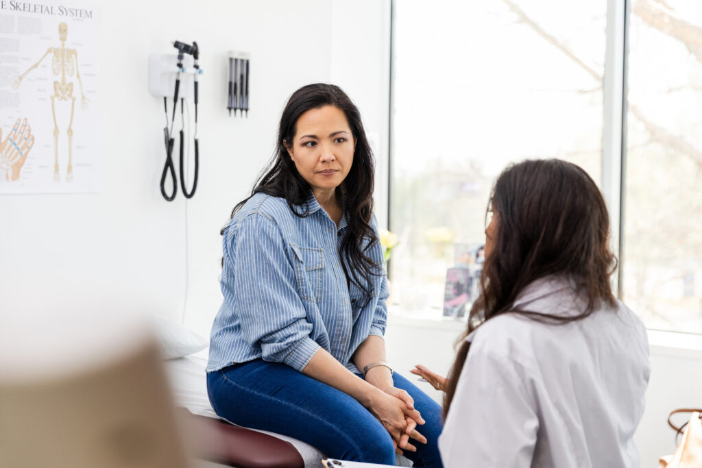 A middle-aged dark-haired woman has a serious but supportive conversation with her female doctor.