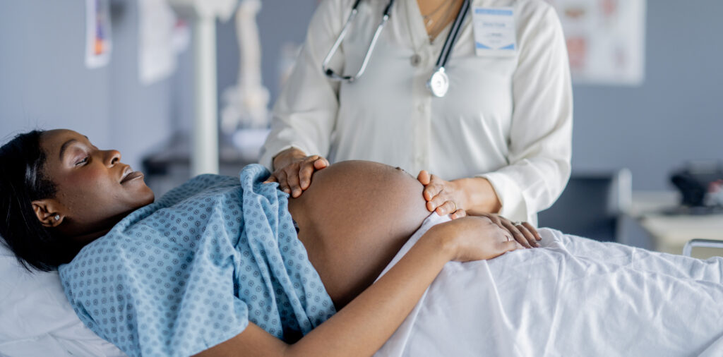 A pregnant woman lays out on an exam table during a prenatal appointment.  Her Obstetrician is checking her growth and measuring baby's development.