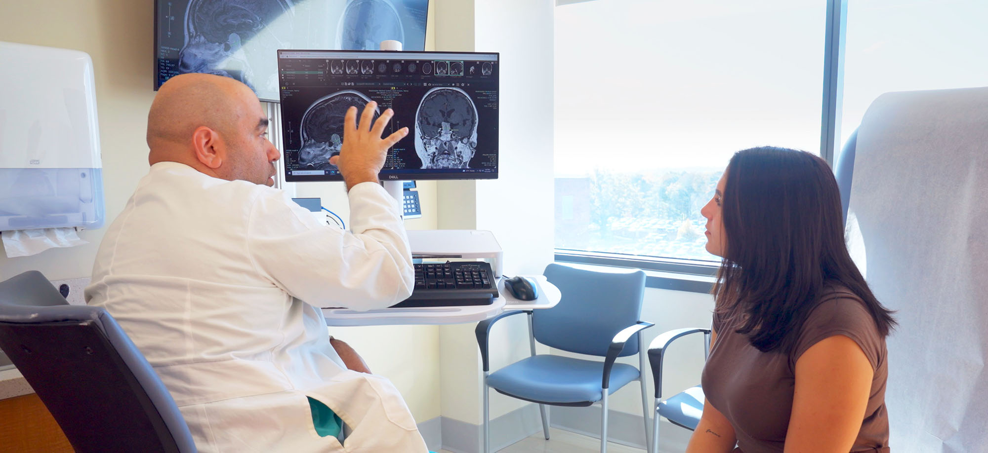 A neuroscience doctor explains a brain image on a computer screen to a female patient in a medical office