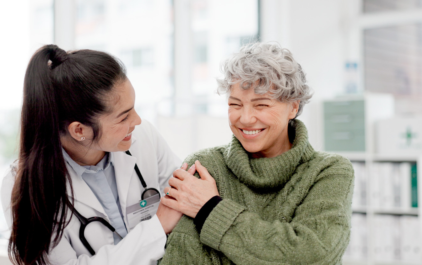 A female healthcare worker shares a joyful moment with her senior female patient in a medical office room.