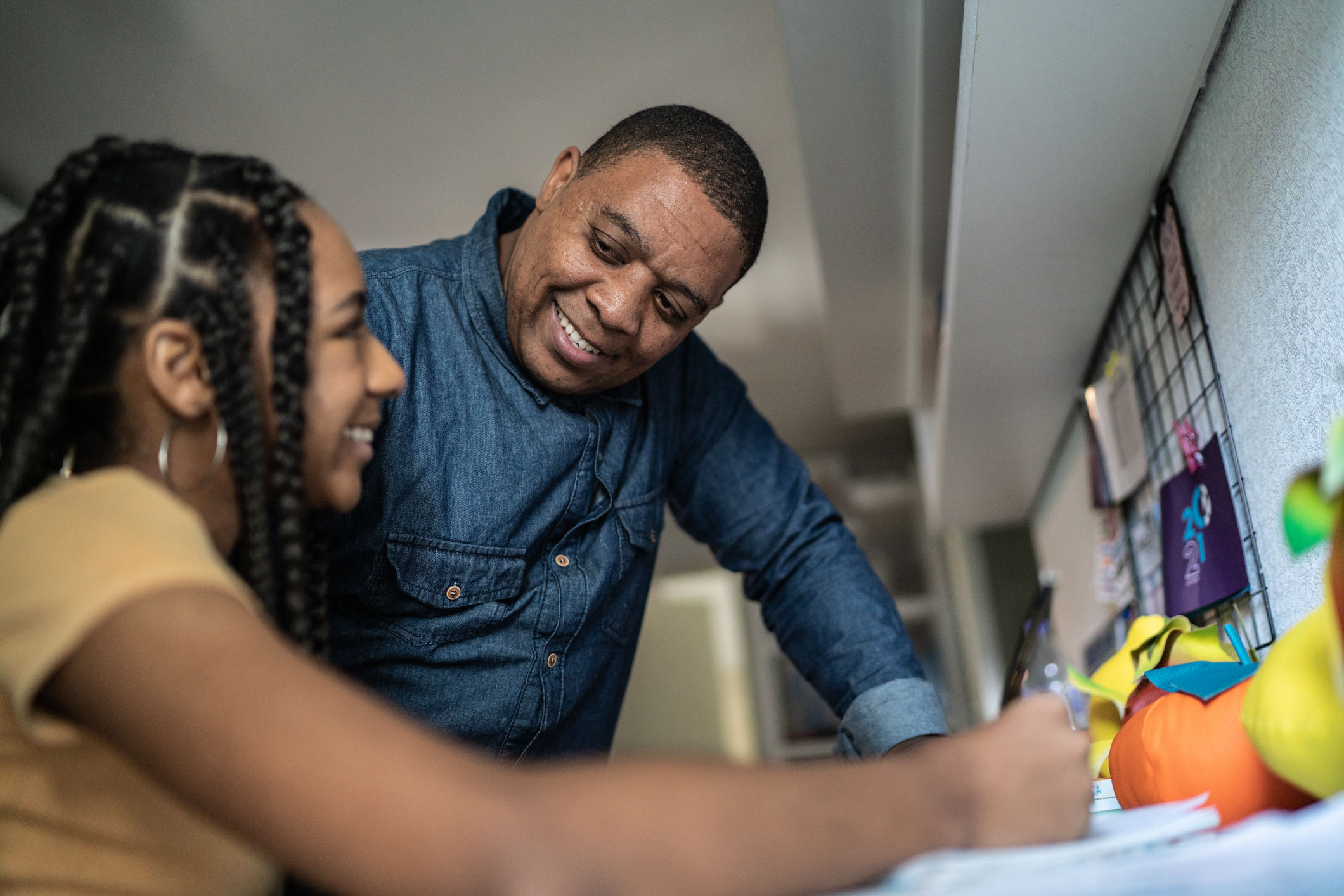 A middle-aged African American dad talks to his teen aged daughter, smiling