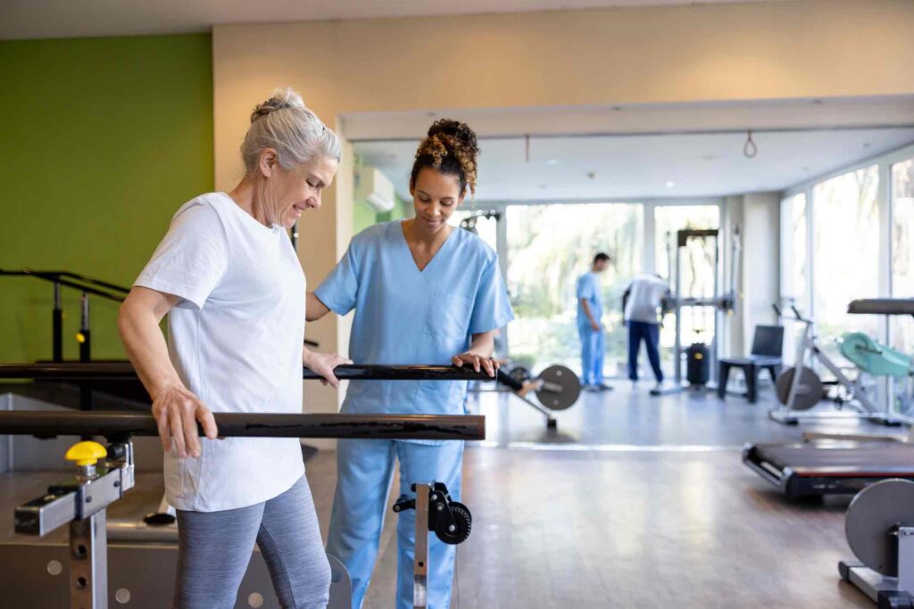 Senior woman in physical therapy walking on the bars with the help of her therapist - orthopedic medicine concepts